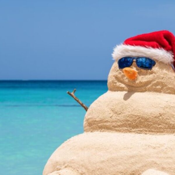 Smiling sandy snowman with red santa hat on the caribbean beach. Holiday concept for New Year and Christmas Cards